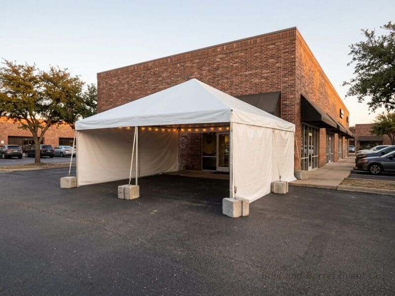 20x20 premium frame tent rental in Midlothian TX with sidewalls and ballast block anchoring set up on a parking lot outside a commercial building