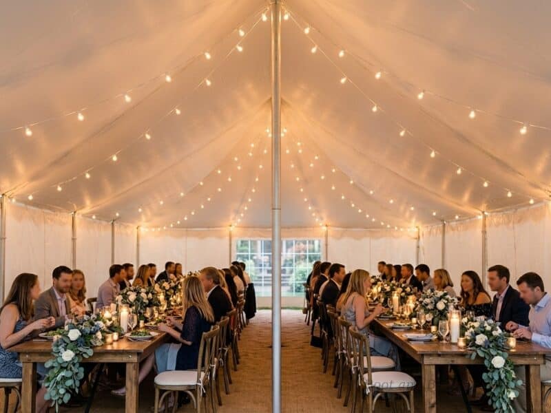 Interior view of a 20x30 high peak pole tent rental in Venus TX with string lights overhead and guests seated at farm tables for a wedding reception