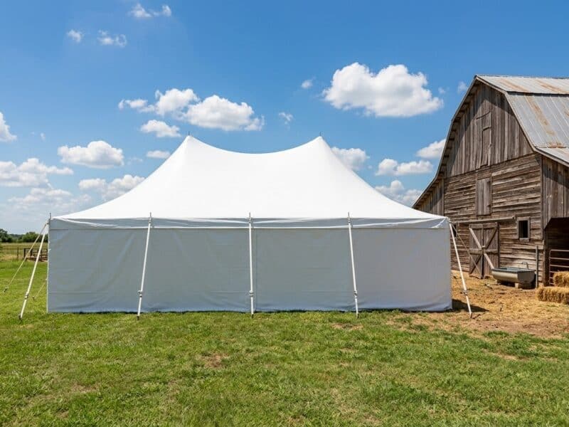 20x30 high peak pole tent rental in Cleburne TX with full sidewalls set up beside a rustic wood barn on a sunny day