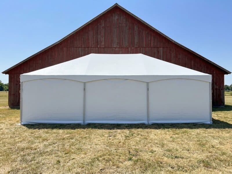 20x40 premium frame tent rental in Crowley TX with partial sidewalls set up beside a weathered gray barn on a summer day