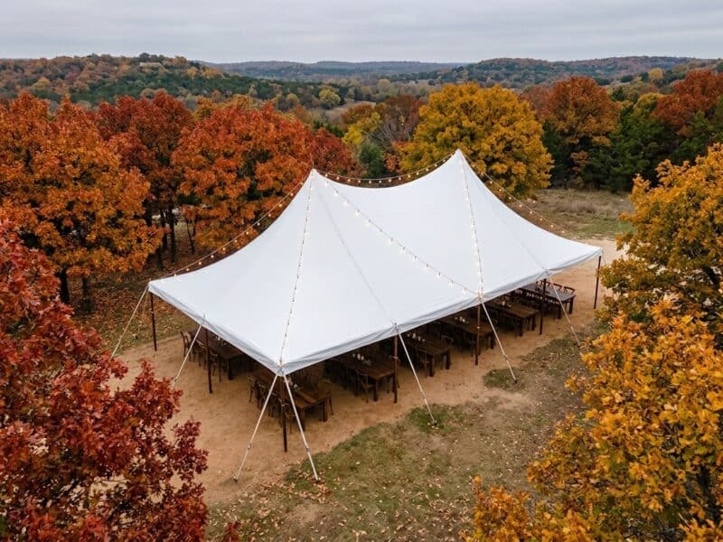 Aerial view of a 20x40 high peak pole tent rental in Cleburne TX with farm tables cross-back chairs and string lights set for a fall outdoor event