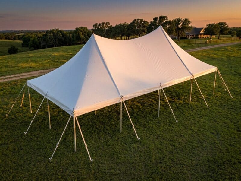 Aerial view of a 20x40 high peak pole tent rental in Grandview TX set up empty on a green ranch pasture at sunset with a farmhouse in the background