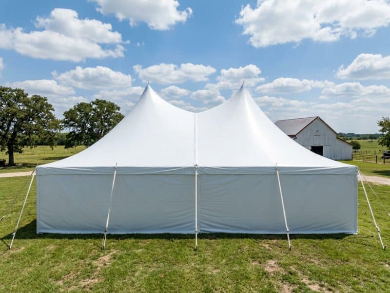 20x40 high peak pole tent rental in Glen Rose TX showing dual peaks and full sidewalls beside a white barn on a ranch property