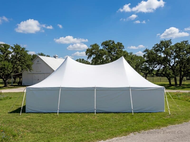 20x40 high peak pole tent rental in Mansfield TX with full sidewalls set up beside a white barn on a sunny Texas ranch