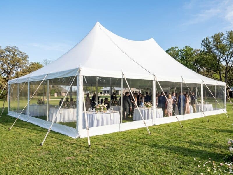30x50 high peak pole tent rental in Venus TX with clear sidewalls and wedding guests mingling inside at a spring outdoor reception