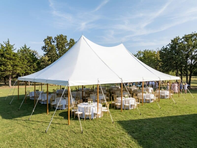 30x50 high peak pole tent rental in Rio Vista TX with gold Chiavari chairs and round tables set for an outdoor wedding reception under Texas oak trees