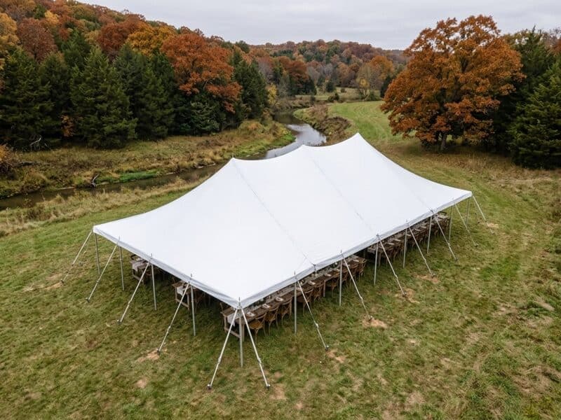 Aerial drone view of 30x60 WIND pole tent with farm tables set along a creek bottom surrounded by fall foliage — Boot & Barrel Event Co. Joshua TX