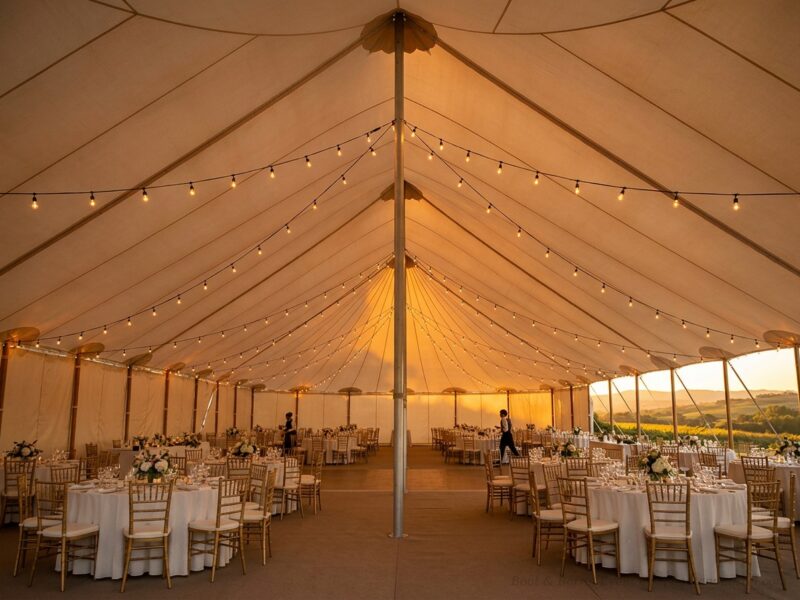 Interior of 30x60 pole tent with center pole and string lights over wedding reception tables and chiavari chairs at golden hour — Boot & Barrel Event Co. Burleson TX