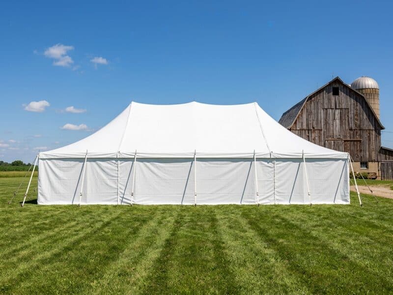 30x60 WIND pole tent fully enclosed with solid white sidewalls next to rustic barn on a sunny day — Boot & Barrel Event Co. Glen Rose TX