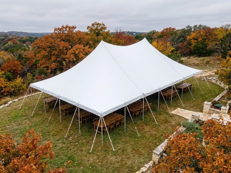 Aerial drone view of 40x60 WIND pole tent with farm tables on a Texas limestone hilltop surrounded by fall foliage — Boot & Barrel Event Co. Weatherford TX