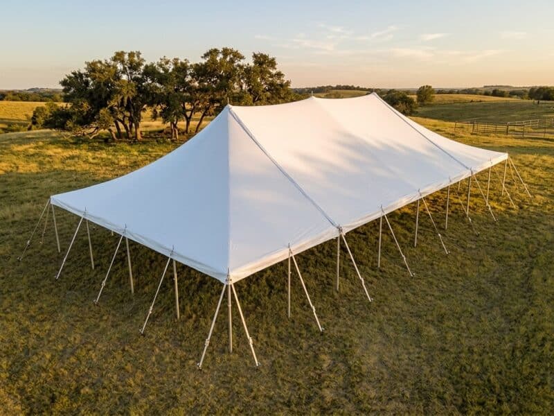 40x60 WIND pole tent open sides at golden hour on a North Texas ranch with green pasture and oak trees — Boot & Barrel Event Co. Rio Vista TX