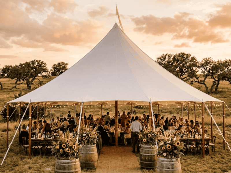 44x43 oval sailcloth tent with wedding reception, farm tables, barrel decor and golden hour Texas sky — Boot & Barrel Event Co. Cleburne TX