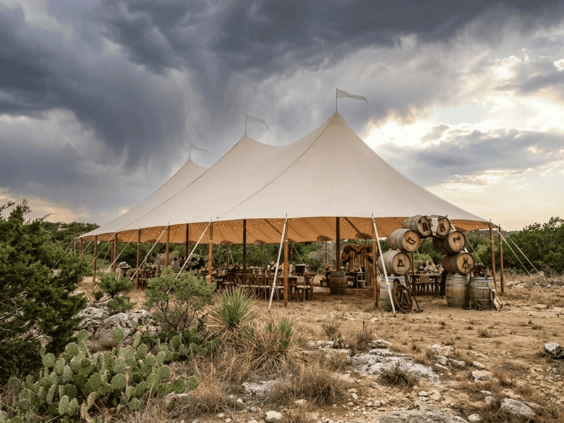 Three-peak sailcloth tent against dramatic stormy Texas sky near Cresson TX, prickly pear cactus, rocky scrubland, barrel arch, open sides, birthday party, Boot & Barrel Event Co.