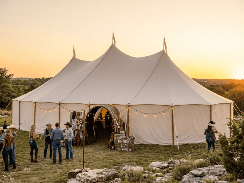 Three-peak sailcloth tent at western birthday celebration at sunset near Glen Rose TX, barrel arch tunnel entrance, cowboy hats, limestone terrain, Boot & Barrel Event Co.