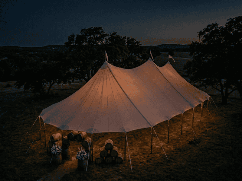 44x83 sailcloth tent with three peaks glowing at night on Texas Hill Country ranch, barrel decor, aerial view, Boot & Barrel Event Co.