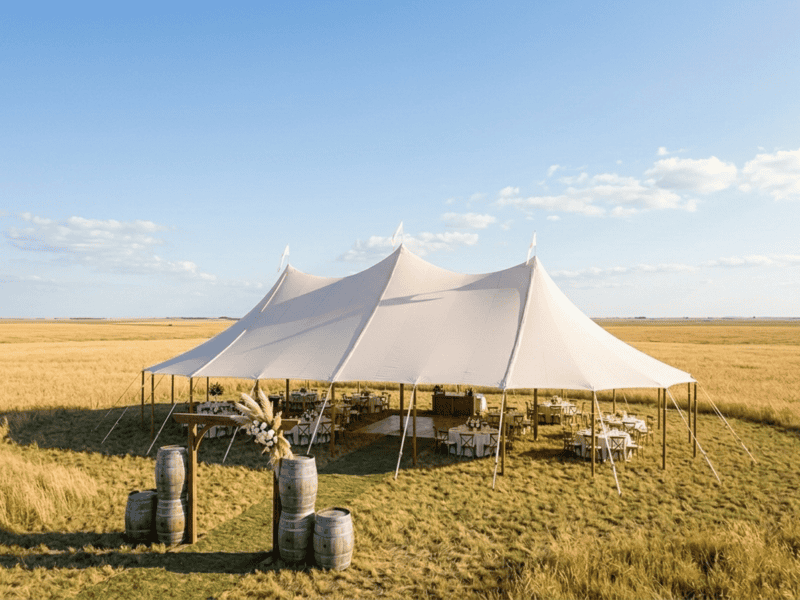 Three-peak sailcloth tent on flat open Texas blackland prairie near Venus TX, golden wheat fields, wide open sky, wine barrel entrance decor, wedding reception setup, Boot & Barrel Event Co.