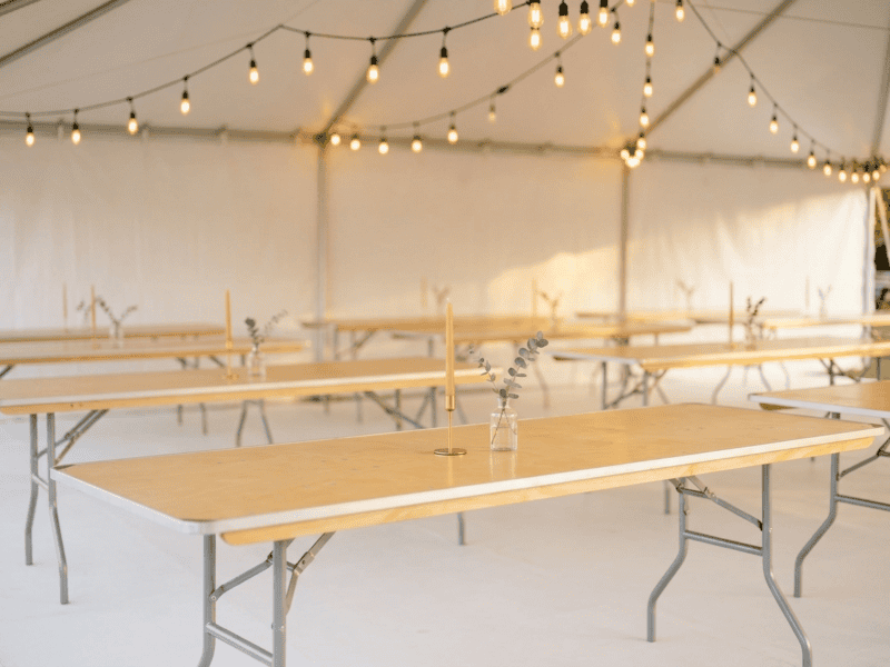 8 foot x 36 inch wide birchwood banquet table showing natural bare wood top with candle and bud vase inside tent in Texas