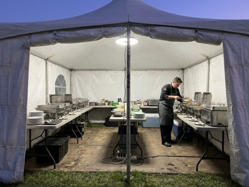 Caterers package tent rental in Godley TX with a chef working a buffet line inside a high peak frame tent at dusk