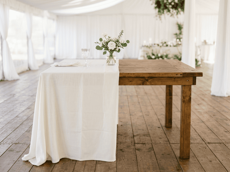 Bar height cocktail farm table with white linen half draped showing hardwood top underneath in Cleburne TX