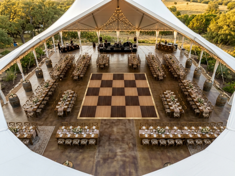 Aerial view of chestnut fruitwood dance floor rental as centerpiece with farm tables in horseshoe layout and Edison string lights — Boot & Barrel Event Co. Joshua TX