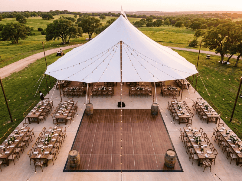 Aerial view of fruitwood dance floor rental as centerpiece of outdoor Texas ranch wedding with farm tables and string lights — Boot & Barrel Event Co. Joshua TX
