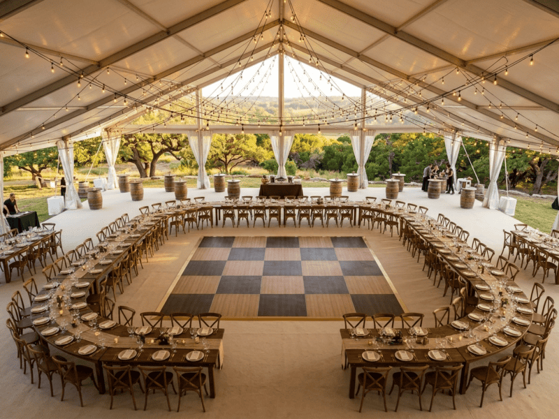 Aerial view of chestnut fruitwood dance floor rental as centerpiece with farm tables in horseshoe layout and Edison string lights — Boot & Barrel Event Co. Keene TX