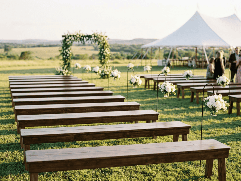 Rustic farm bench wedding ceremony seating on Texas ranch with floral arch