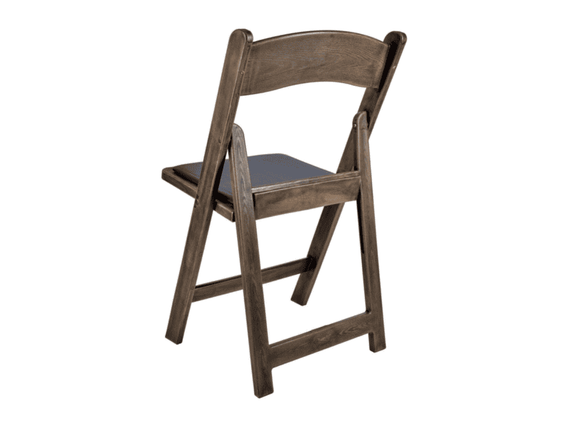 Fruitwood WoodGrain resin folding chair at an angle with black cushion rental in Alvarado TX — Boot & Barrel Event Co.
