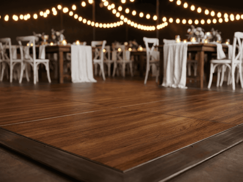 Close up of fruitwood portable dance floor surface with elegant wedding reception setup softly blurred in background — Boot & Barrel Event Co. Weatherford TX