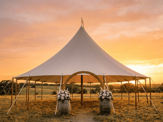 44x43 sailcloth tent with single soaring peak and barrel arch entrance with white floral arrangements at golden hour sunset near Cleburne TX, Boot & Barrel Event Co.