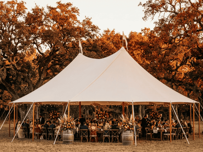 sailcloth tent fall wedding reception with autumn orange foliage, burnt orange floral barrel decor and guests dining in Texas