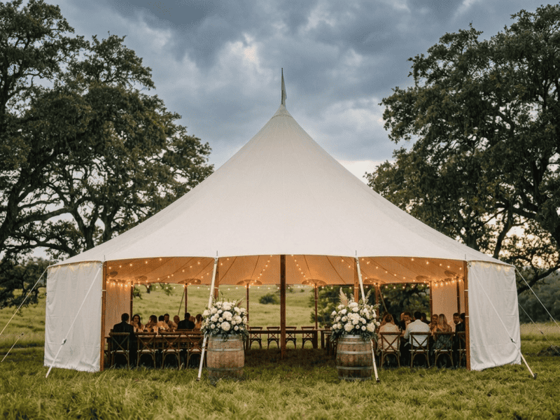 44x63 sailcloth tent with white sidewalls down during rain showing weather protection, guests dining inside with string lights and barrel decor