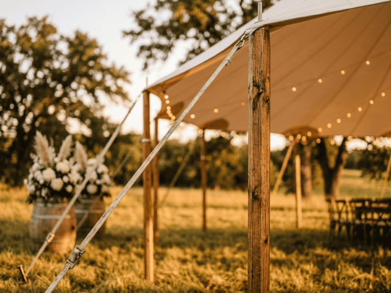 Close up detail of sailcloth tent wooden side pole, catenary eave curve, guy wire and barrel with white floral arrangement at golden hour