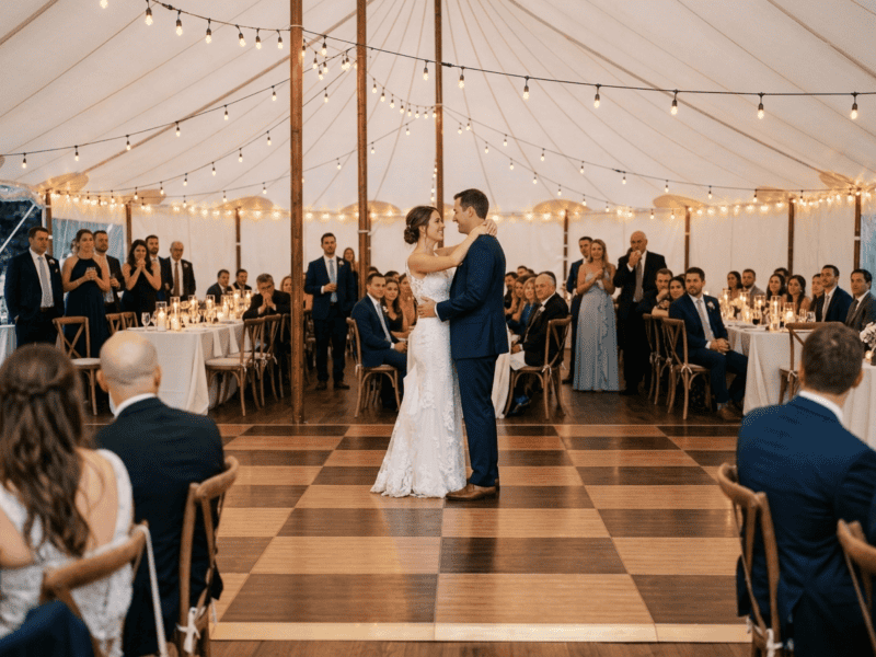 Bride and groom first dance on chestnut fruitwood two-tone dance floor rental under white tent with Edison string lights — Boot & Barrel Event Co. Mansfield TX