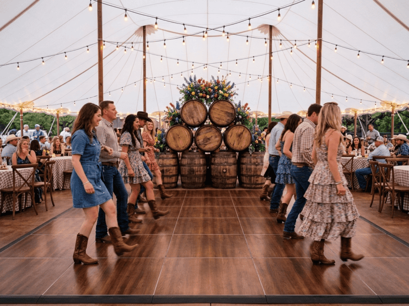 Fruitwood portable dance floor rental at a western Texas barn dance with line dancing and whiskey barrel decor — Boot & Barrel Event Co. Alvarado TX